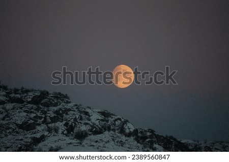 A near full moon is slowly creeping behind a mountain along the norwegian coast on an early winter morning near the town of Bodo.