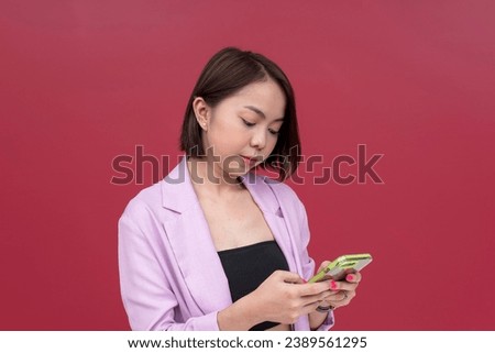 A smiling young asian woman in her mid 20s sporting short hair chatting on her cellphone. Wearing a pink blazer and black tube top. Studio shot with burgundy background.