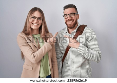 Young couple standing over white background cheerful with a smile of face pointing with hand and finger up to the side with happy and natural expression on face 