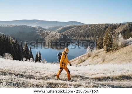 Man with backpack walking on the mountains against the background of an icy lake, mountain trekking in winter, cold season, outdoor vacation, autumn hike. High quality photo