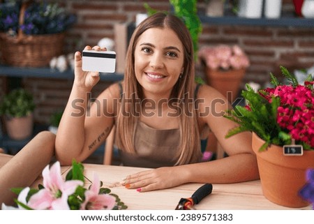 Young blonde woman working at florist shop holding credit card looking positive and happy standing and smiling with a confident smile showing teeth 