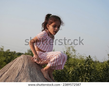 Cute little girl slipping on hill.Wearing pink dress outdoor in park.Close up hands with comedy action.Portrait image blur background.