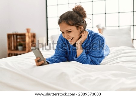 Young beautiful hispanic woman using smartphone lying on bed at bedroom