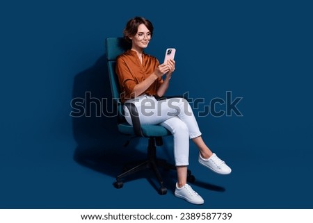 Full size photo of pretty young girl sit armchair hold device dressed stylish brown blouse isolated on dark brown color background