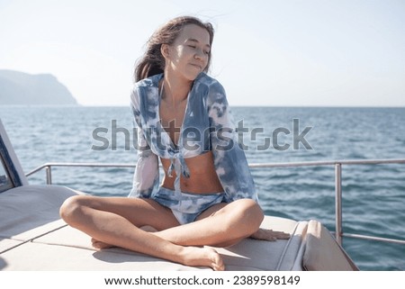  A beautiful young girl with a slender figure travels and rests on a boat during a summer vacation in the open sea or ocean A model is wearing a blue swimsuit .