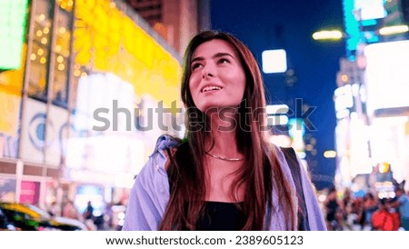 Portrait of joyful attractive Caucasian woman on Times Square, USA. Cute beautiful happy girl looking at buildings wearing stylish clothes with lots of people and cars on background.