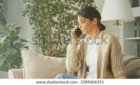 Young beautiful woman relaxing on the sofa, talking on the phone and contact. Mobile communication app using smartphone. Lady spending time at home with cell gadget technology