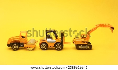 Toy forklift, asphalt paver and excavator on yellow background