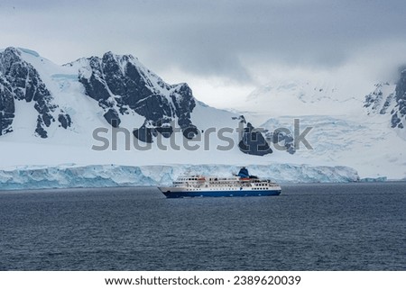 A large sailboat  pictured in front of a stunning backdrop of snowy mountainous terrain in Antarctica
