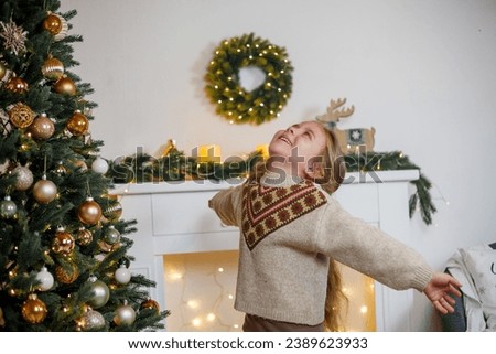 An adorable little girl of 5 years old with long curly hair and blue eyes decorates a Christmas tree. Holidays. New Year.
