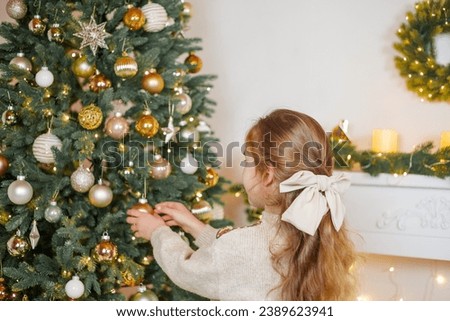 An adorable little girl of 5 years old with long curly hair and blue eyes decorates a Christmas tree. Holidays. New Year.