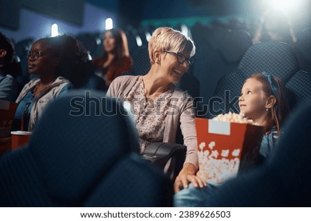 Happy senior woman and her granddaughter communicating while watching movie in cinema.
