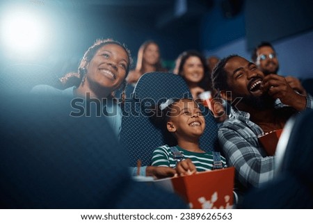 Cheerful African American family having fun while watching movie in a theater.
