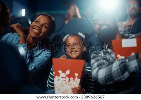 Happy African American girl with parents watching movie in cinema.