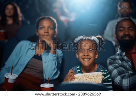African American family enjoying in movie projection in theater. Focus is on happy girl. 