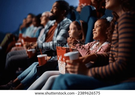 Happy African American girl eating popcorn while watching movie with her family in theater. 
