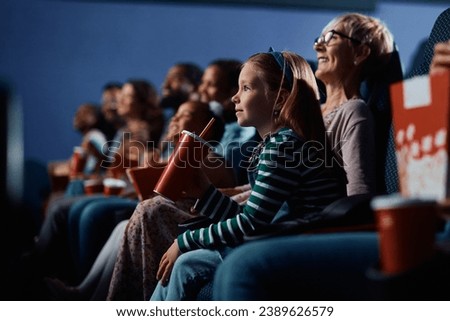 Small girl enjoying in movie projection while being with her grandmother at the cinema.