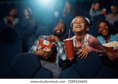 Happy African American girl enjoying during movie projection in cinema.