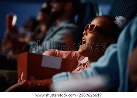 African American girl wearing 3D eyeglasses while watching movie in cinema.