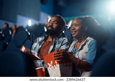 African American couple enjoying in movie projection in cinema.  Royalty-Free Stock Photo #2389626637