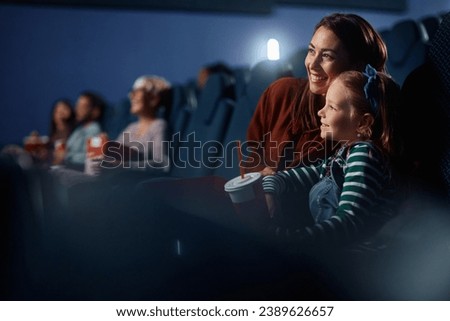 Happy little girl and her mother watching movie in cinema. Copy space.