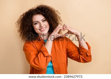 Photo portrait of pretty young girl show love gesture heart hands wear trendy orange outfit isolated on beige color background