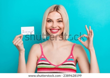Photo portrait of pretty young girl hold credit card showing okey dressed stylish striped outfit isolated on aquamarine color background