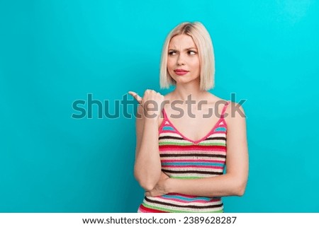 Photo portrait of pretty young girl point look skeptical empty space wear trendy striped outfit isolated on cyan color background