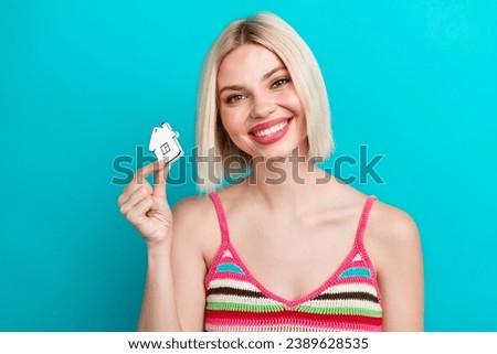 Photo of satisfied young lady hold small house toy miniature building showing her dream apartment isolated on aquamarine color background