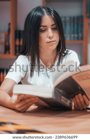 A shallow focus shot of an attractive brunette girl reading a book in a library