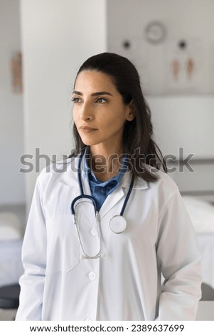 Serious pensive young Latin doctor woman in white coat and stethoscope on neck looking away in deep thoughts, thinking on medical profession, career in medicine, difficult patients case