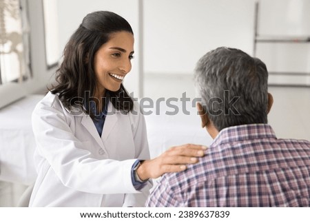Happy young doctor woman enjoying medical job, giving support to older patient, talking to man for healthcare examination, checkup, touching shoulder with support, sympathy Royalty-Free Stock Photo #2389637839