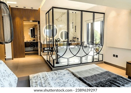 Modern and spacious bedroom with open bathroom concept, featuring a freestanding tub, large windows, and wooden accents. Royalty-Free Stock Photo #2389639297