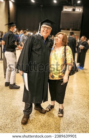 A senior citizen receiving an advanced degree is congratulated by the woman on his left. Royalty-Free Stock Photo #2389639901