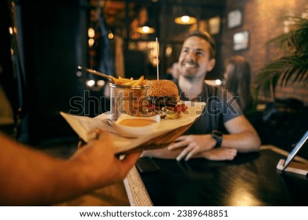 Cropped picture of a hand bringing food to a man in restaurant in a blurry background.