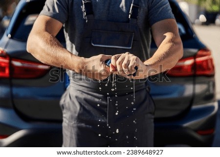 Worker's hands squeezing a wet rag at car wash station. Royalty-Free Stock Photo #2389648927