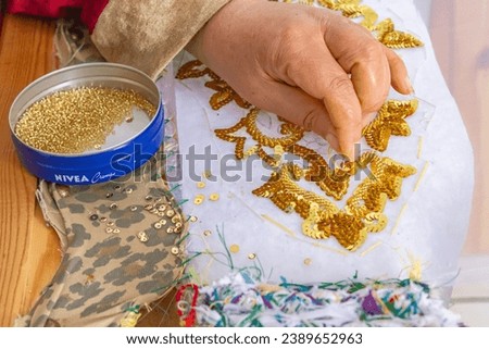 Raf Raf, Bizerte, Tunisia. A Tunisian woman embroidering gold sequins onto white cloth. Royalty-Free Stock Photo #2389652963