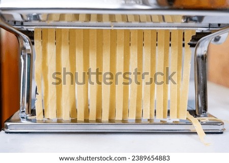 Preparing homemade pasta with a pasta machine. Preparing tagliatelle with a pasta machine on the kitchen counter. Close-up.