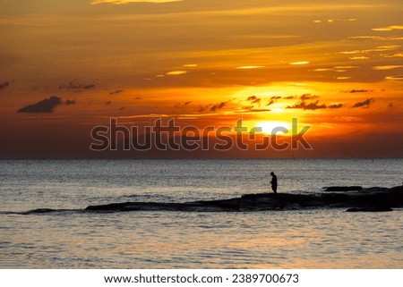 A man stands fishing on the seashore at Mae Ramphueng Beach in Rayong Province, Thailand.Silhouette picture style.
