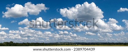 Panoramic view of the blue sky slightly overcast with cumulus clouds, cumulus clouds or fair weather clouds and fleecy clouds above the horizon with houses, fields and woodland Royalty-Free Stock Photo #2389704439