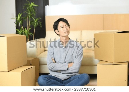 A young Asian man thinking in front of a large number of cardboard boxes
