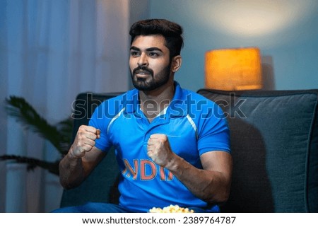 Excited young man in Indian cricket jersey waiting for match win at home - concept of championship, entertainment and tournament.