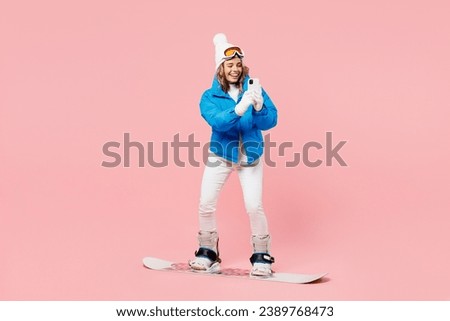 Snowboarder fun woman wear blue suit goggles mask hat ski padded jacket take photo on mobile cell phone isolated on plain pastel pink background. Winter extreme sport hobby weekend trip relax concept