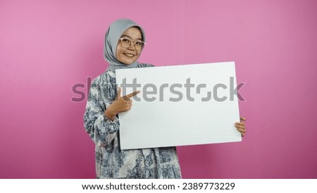 Young hijab Muslim woman holding blank banner, placard, chalkboard, blank sign, white billboard, presenting something on copy space, promotion