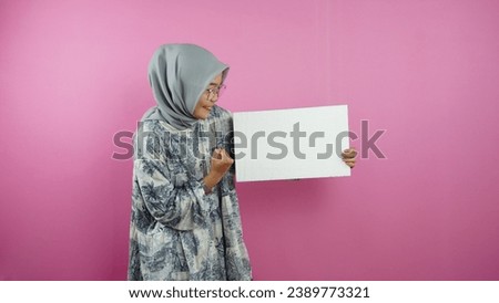 Young hijab Muslim woman holding blank banner, placard, chalkboard, blank sign, white billboard, presenting something on copy space, promotion