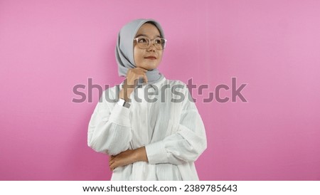 Portrait of an Asian Muslim woman posing wearing a white shirt and hijab standing isolated on a pink background