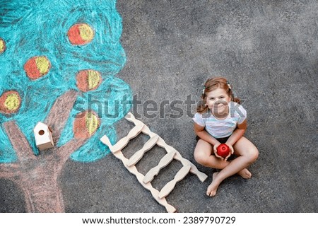 Cute little girl painting with colorful chalks apples harvest from apple tree on asphalt. Cute preschool child with having fun with chalk picture. Creative leisure for children, drawing and painting.