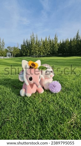 Vertical picture of pink stuffed elephant toy and a stuffed white poodle dog sat happily together on the bright green lawn in the warm morning sunshine. 