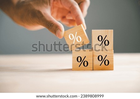 Concept of interest rate and financial rates. Hand placing a wooden cube block on top, symbolizing an increase, with an upward direction icon and percentage symbol. Royalty-Free Stock Photo #2389808999
