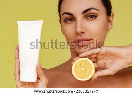 Beautiful woman holds tube with cosmetic cream and lemon. Photo of attractive woman with perfect makeup on  yellow  background. Beauty concept